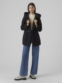 Fekete kapucnis kabát dupla gombolásos kialakítással, ezüst gombokkal és elülső zsebekkel. Magasan derekú kék farmernadrággal és ezüst cipővel párosítva.