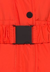 Oranžová vypodložená bunda se staženým páskem, se skládacím černým plastovým sponou a kulatým černým knoflíkem na zapínání.