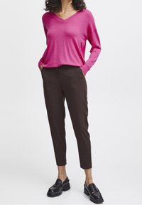 Pull rose à col en V avec manches longues et coupe décontractée, associé à un pantalon marron slim et des mocassins noirs à plateforme.