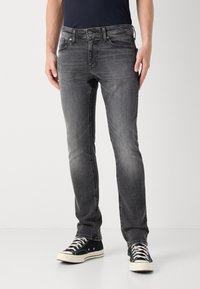 Grey denim jeans with a slim fit design, featuring five pockets, subtle distressing, and paired with black canvas sneakers.