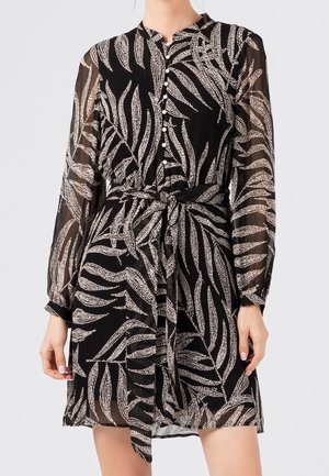 Robe noire avec de longues manches transparentes, présentant un motif de feuilles en blanc. Devant boutonné avec un lien à la taille, créant une silhouette ajustée.