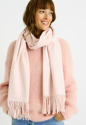 Bufanda rosa claro hecha de material suave, con bordes con flecos. Llevada sobre un suéter rosa claro con textura; el diseño es simple y contemporáneo.