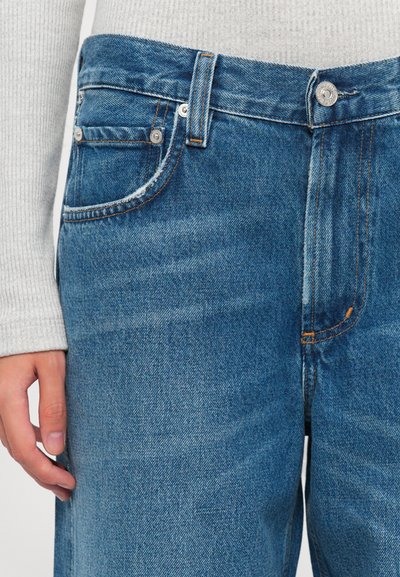 Close-up of a person's hand near the pocket of blue denim jeans worn with a light gray ribbed sweater.