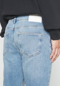 Lichtblauwe denim jeans met een relaxte pasvorm, voorzien van een witte leren patch op de tailleband en dubbele gestikte achterzakken.