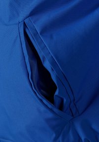 Tessuto blu con una texture liscia presenta una tasca a fessura con bordi curvi, cuciture a vista e una fodera parzialmente visibile.