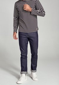 Marinblå och vit randig långärmad skjorta med rund halsringning, ihopparad med mörka jeans och vita sneakers. Uppvikta jeans visar grå tygdetaljer.