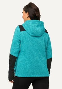 Giacca in pile turchese con cappuccio, dettagli neri su spalle e maniche, tessuto testurizzato e vestibilità casual, vista da dietro.