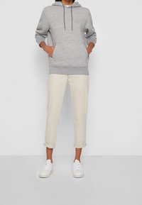 Sweat-shirt à capuche gris avec une poche avant, associé à un pantalon crème retroussé et des baskets blanches. Coupe décontractée et ample.