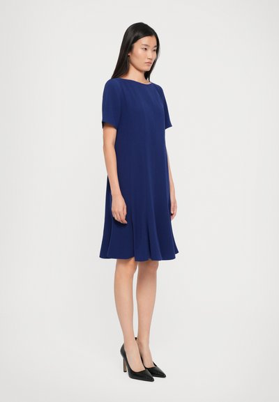 Rochie bleu marin cu mâneci scurte, croială lejeră, fustă evazată și textură netedă; asortată cu pantofi cu toc înalt negri.