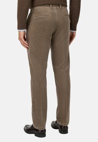 Pantaloni in corduroy marrone con taglio dritto, caratterizzati da schemi a coste verticali sottili e tasche posteriori, abbinati a scarpe nere.