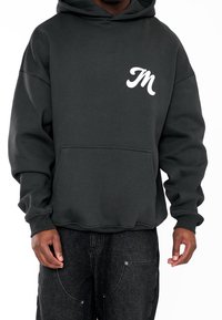 Tmavě šedá mikina s kapucí a přední kapsou, s bílým vyšívaným logem "M" na levé straně hrudi. Hladká textura, volný střih.