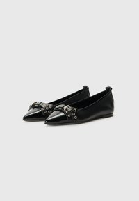 Ballerines en cuir noir avec un design à bout pointu, comportant une sangle décorative avec des œillets en argent et une boucle sur le coup de pied.