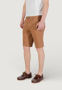 Shorts en coton marron avec une coupe slim, dotés d'une fermeture à bouton et de poches à l'avant, associés à des chaussures bateau en cuir marron foncé.