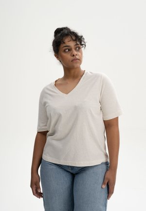 Beige V-Ausschnitt T-Shirt mit kurzen Ärmeln, aus weichem Material gefertigt. Kombiniert mit hellblauen Jeans, die einen lässigen Schnitt und eine dezente Textur aufweisen.
