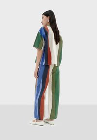 Bunt gestreiftes Baumwoll-Outfit mit einem kurzärmeligen Oberteil und einer lockeren, weiten Hose in Blau, Grün, Rot und Creme. Weiße Schuhe.