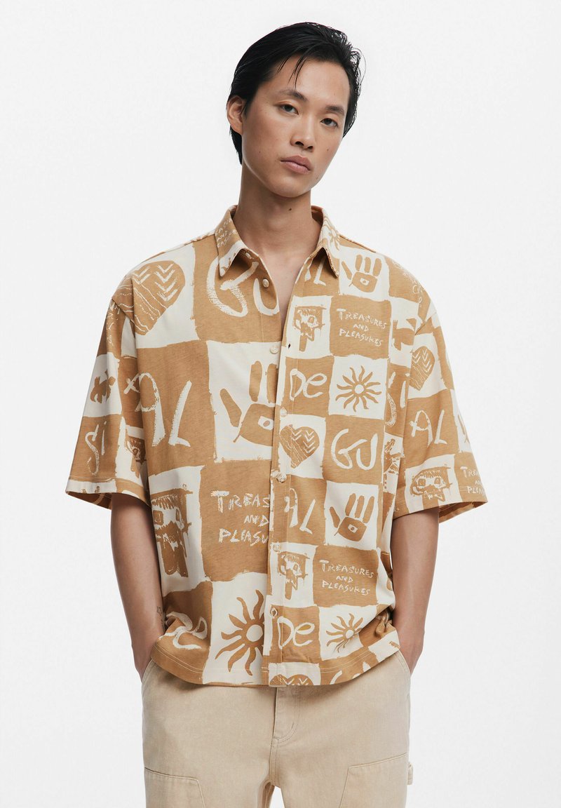Kortærmet skjorte med knaplukning i beige med abstrakte brune mønstre. Har en afslappet pasform og blød tekstur.