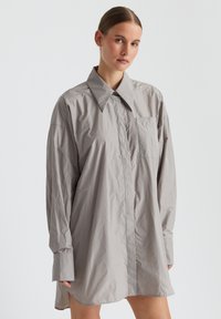 Hellgraues, oversized Hemdkleid mit spitzem Kragen, langen Ärmeln, vorderem Knopfverschluss und einer einzigen Brusttasche. Glatte Textur.