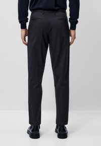 Svarta byxor i slim fit med två bakfickor och en mjuk textur, matchade med svarta läderankelboots.