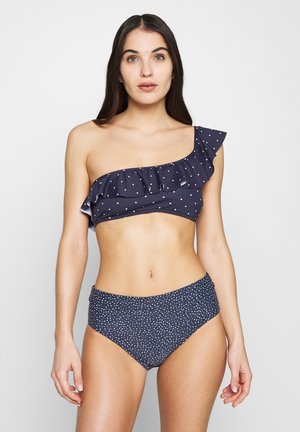 Navy bikini set with white polka dots; one-shoulder top features ruffle detail; high-waisted bottom with a smooth texture.