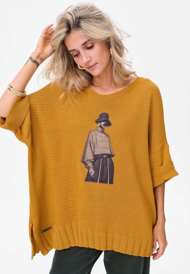 Musztardowożółty sweter dziergany o luźnym kroju, z nadrukiem przedstawiającym postać w ubraniu w paski na przodzie.