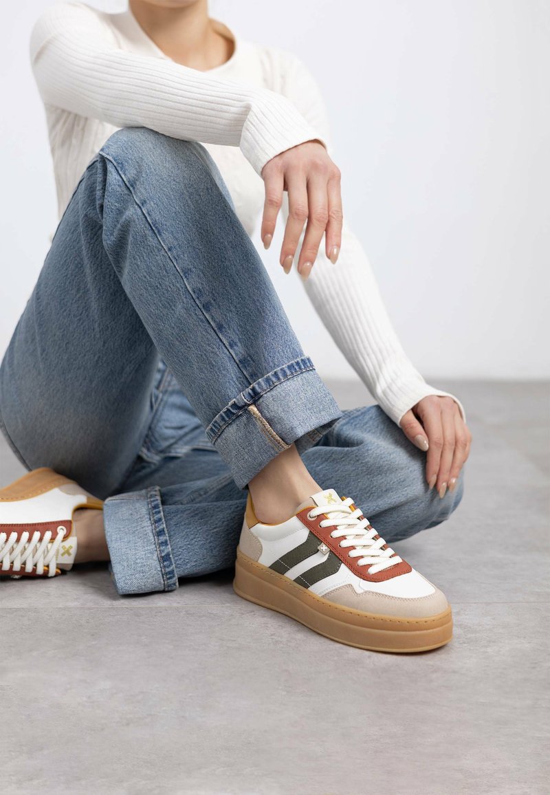 Sneaker con tomaia bianca, strisce marroni e verdi, dettagli gialli e suola piatta marrone chiaro. Presentano lacci e materiale testurizzato.