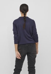 Granatowy sweter z prążkowanymi mankietami, zestawiony z czarnymi dżinsami. Sweter ma okrągły dekolt i gładką, dzianinową strukturę.