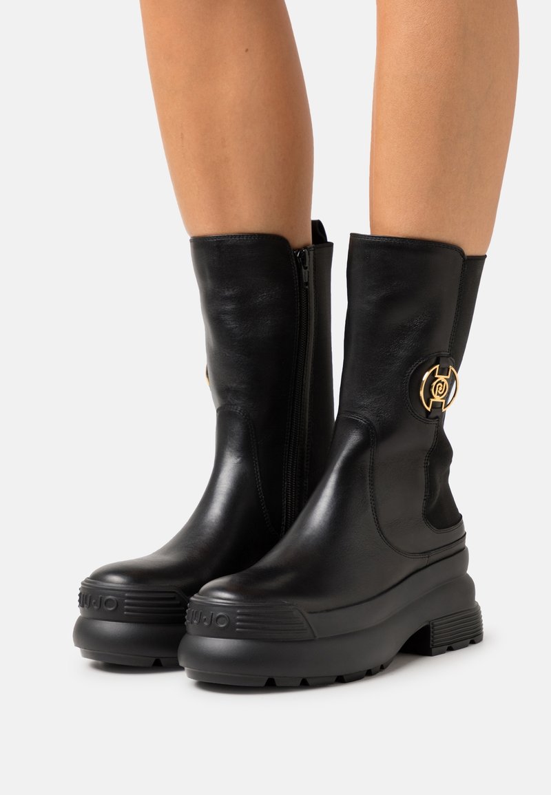 Black leather ankle boots with a side zipper and gold accent hardware. Features a chunky black rubber sole with textured details.