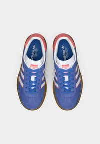 Par med blå Adidas-sneakers med hvite striper, korallfargede hældetaljer, blå skolisser og gummisåler, sett ovenfra på en hvit bakgrunn.