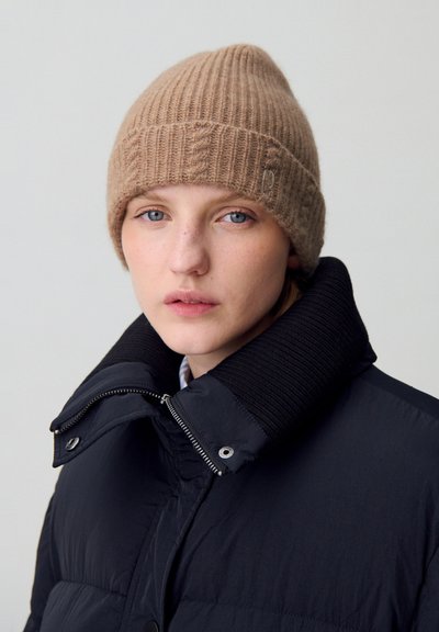 Berretto di lana marrone lavorato a maglia con texture a costine e un piccolo logo, abbinato a un giubbotto imbottito nero con colletto ripiegato e dettagli con zip.