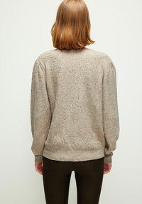 Hellbrauner Pullover mit glitzernden goldenen Flocken, gerippten Bündchen und Saum. Weicher Stoff und lockere Passform mit dezenten Puffärmelchen an den Schultern.