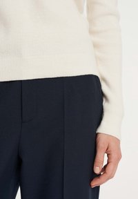 Un maglione a coste color crema si abbina a pantaloni blu su misura. Il maglione ha una vestibilità aderente, mentre i pantaloni presentano una texture liscia con tasche laterali.