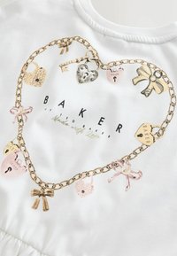 Biele tričko s návrhom zlatej reťaze obsahujúcej rôzne zámky, mašle a kľúč. Logo „BAKER“ vytlačené čiernou farbou v strede.