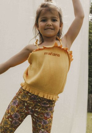 Een gele geribbelde tanktop met ruches en geborduurde tekst, gecombineerd met gebloemde leggings in oranje, paars en bruin.