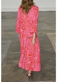 Longue robe rose arborant des motifs rouges et roses audacieux ressemblant à des impressions animales, avec des manches larges et une coupe décontractée.