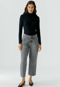 Schwarz langärmliges Turtleneck-Oberteil kombiniert mit hochgeschnittenen, hellgrauen, geraden Jeans. Model trägt schwarze spitze Ballerinas.