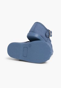 Sininen kangaskengä, jossa on tekstuuroitu pinta, säädettävä hihna metallisoljella ja kiinteä sininen kumipohja.