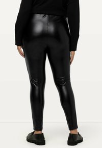 Leggings en simili cuir noir avec une taille haute, une texture lisse et une coupe slim. Associés à des chaussures noires pour un look harmonieux.