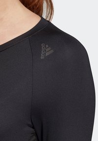 Svart sporttop med en slät yta, med V-hals och subtil Adidas-logotyp på axeln. Skräddarsydd passform designad för rörlighet.