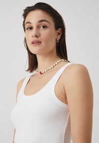 Beaded necklace featuring white flower patterns, red accent bead, and a smooth finish, worn over a white tank top.