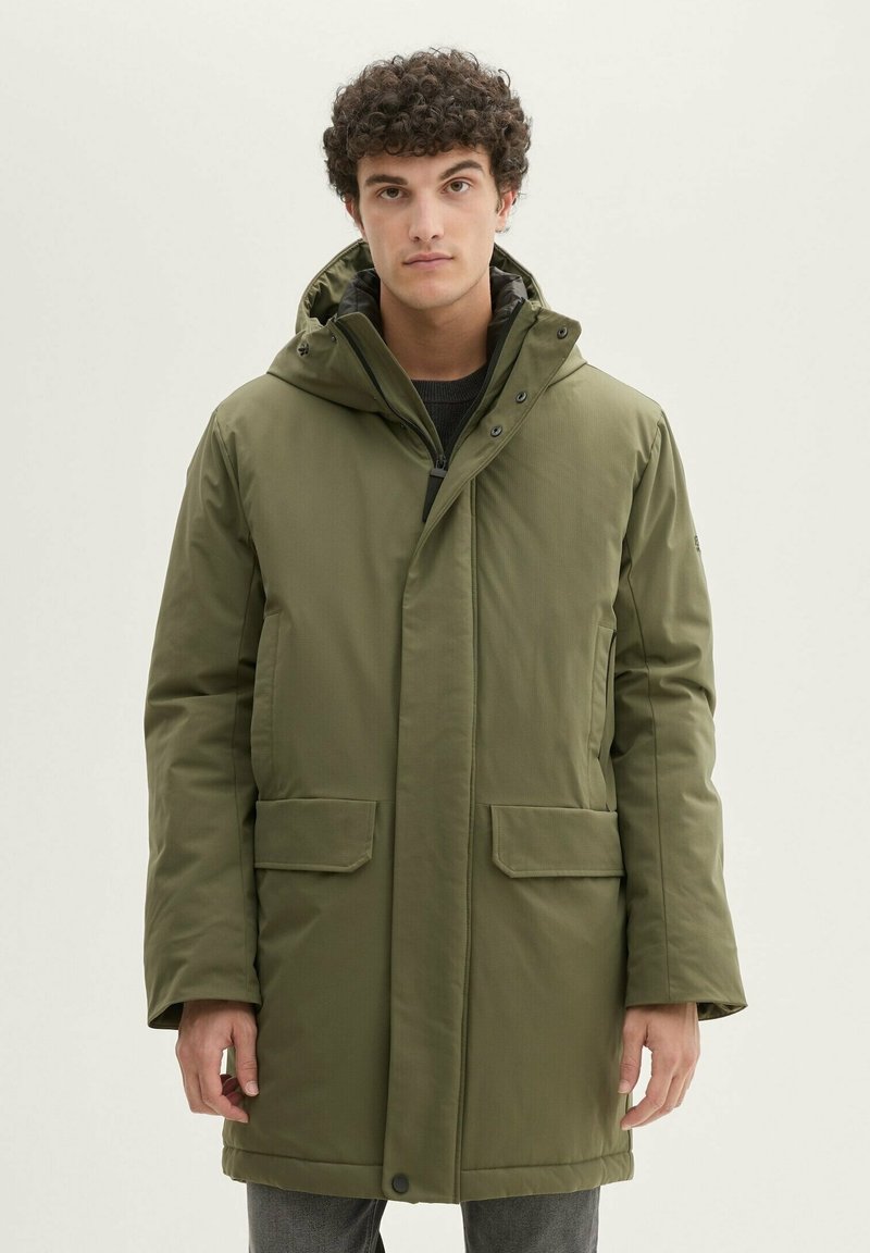 Giacca parka verde oliva con cappuccio, chiusura frontale con bottoni a pressione e zip, due tasche utilitarie e una texture trapuntata.