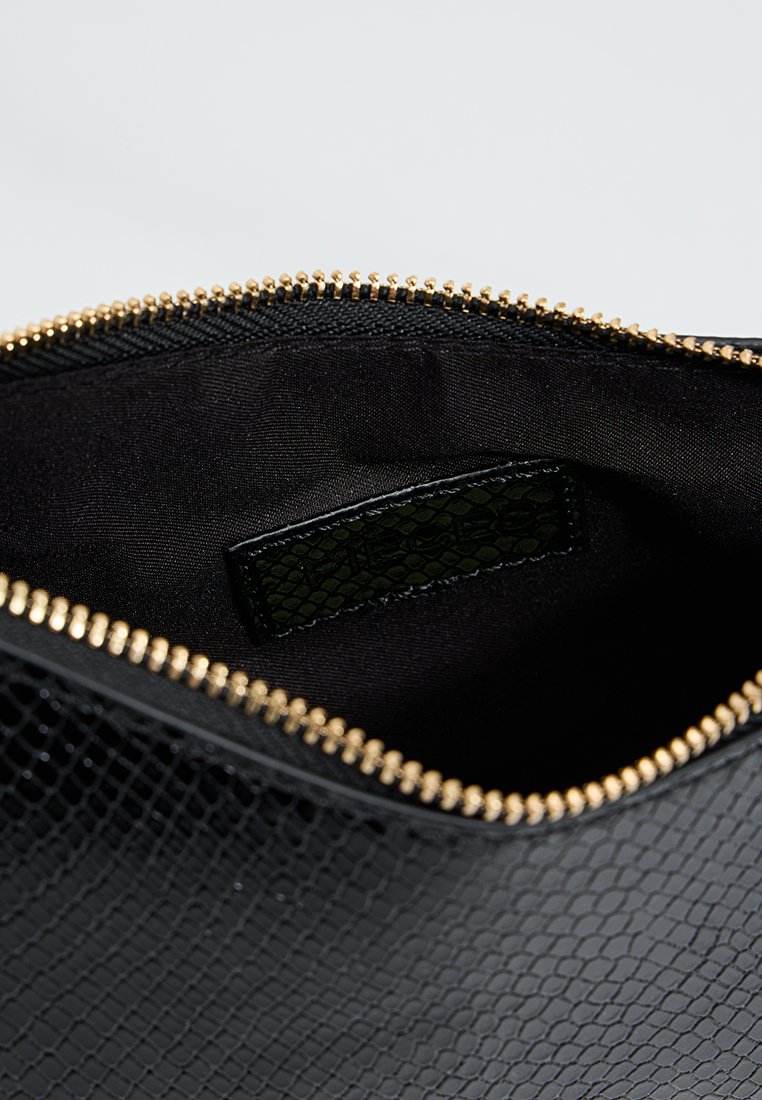 Pochette en cuir texturé noir avec fermeture éclair dorée, ouverte pour montrer un intérieur en tissu noir lisse et une petite poche intérieure.