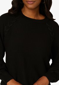 Maglione nero a maglia con collo rotondo, motivo a foglia strutturato sulle spalle e polsini a costine. Tessuto morbido con silhouette aderente.