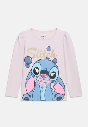 Svetloružová košeľa s dlhým rukávom s veľkým kresleným obrázkom Stitcha, ktorý fúka ružovú bublinu, a nad ňou trblietavý zlatý nápis „Stitch“.