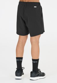 Svarta sportshorts med elastisk midja, sidofickor och en liten vit etikett på baksidan. Bärs med svarta strumpor som har vit text och sneakers.