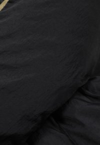 Sort stof med en let krøllet tekstur, der har et blødt og glat udseende, dækker overfladen. Ingen tydelige mønstre eller detaljer synlige.