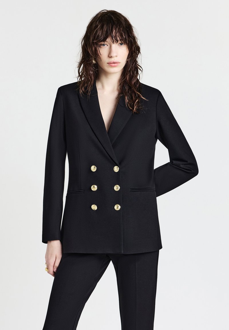 Blazer doppiopetto nero con bottoni dorati, rever a punte e tasche laterali. Design semplice con spalle strutturate e texture liscia.