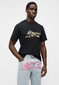 Μαύρο βαμβακερό μπλουζάκι με παραλλαγή γραφικό τίγρη. Ανοιχτό μπλε τζιν παντελόνι με φωτεινό ροζ γραφικό γάτας στο μηρό.