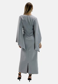 Lungo abito grigio con maniche a campana, texture liscia e spacco sul retro. Presenta una zip nascosta sul retro e un design elegante.