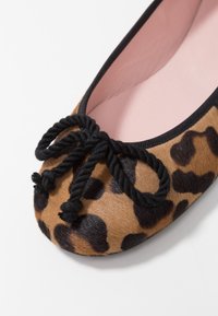 Ballerines en imprimé léopard avec un nœud en corde noire, un dessus en texture douce, un intérieur rose et des bords noirs le long de l'ouverture.