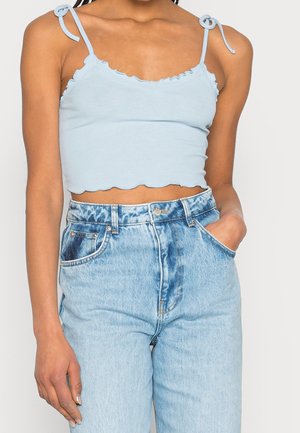 Jasnoniebieski prążkowany top crop z falbaniastymi brzegami i wiązanymi ramiączkami, w połączeniu z jasnoniebieskimi dżinsami o wysokim stanie z przednimi kieszeniami.